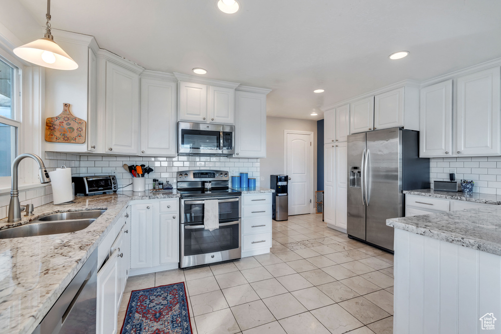 Kitchen with decorative backsplash, appliances with stainless steel finishes, sink, white cabinets, and hanging light fixtures