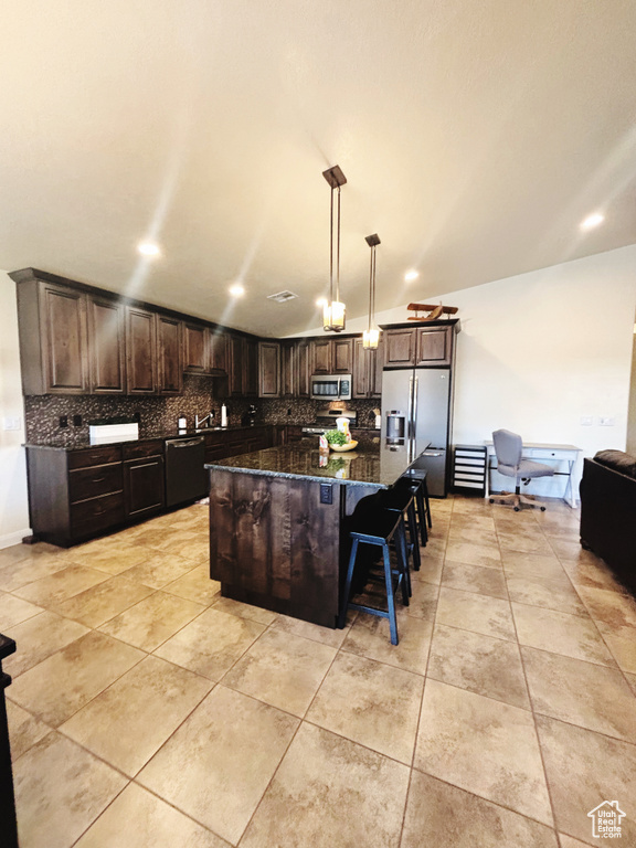 Kitchen featuring decorative backsplash, appliances with stainless steel finishes, dark stone counters, decorative light fixtures, and a kitchen island