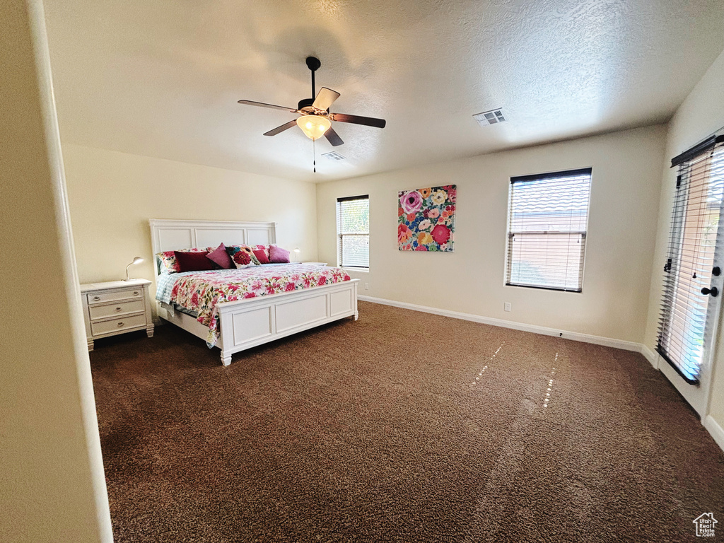 Carpeted bedroom featuring a textured ceiling, multiple windows, and ceiling fan