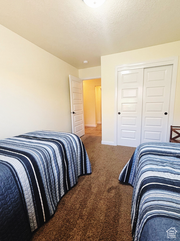 Carpeted bedroom featuring a textured ceiling and a closet