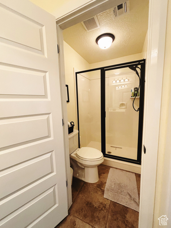 Bathroom featuring a textured ceiling, an enclosed shower, and toilet