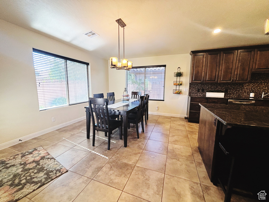 Tiled dining room featuring a healthy amount of sunlight and an inviting chandelier