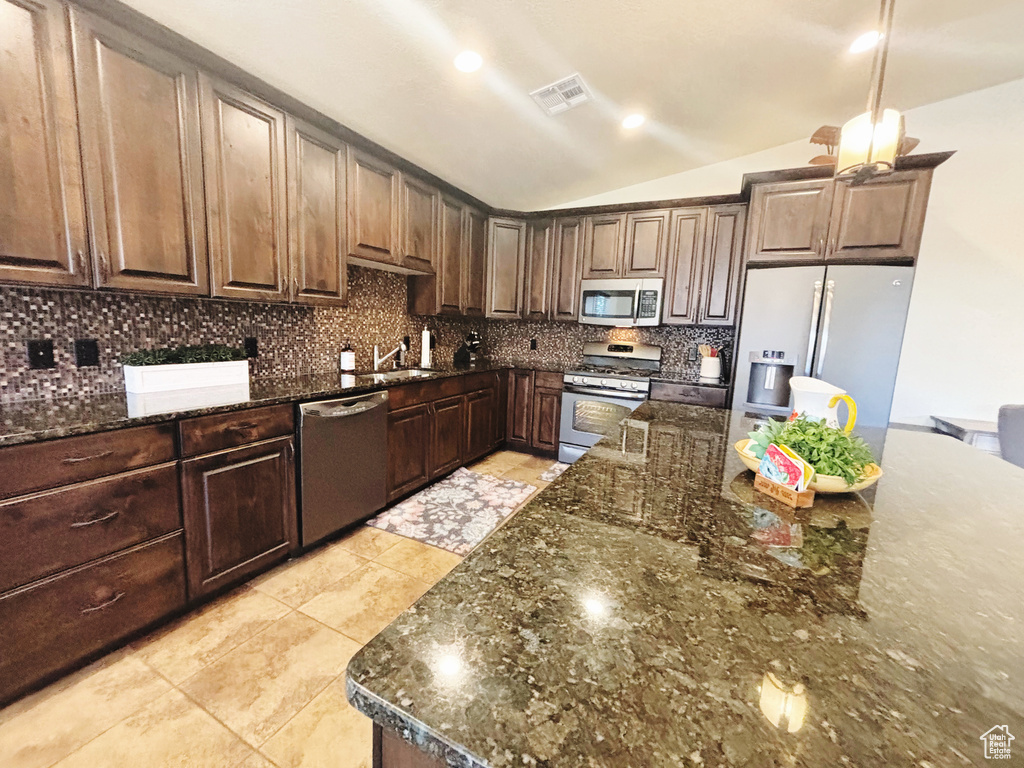 Kitchen featuring appliances with stainless steel finishes, dark stone counters, tasteful backsplash, and lofted ceiling