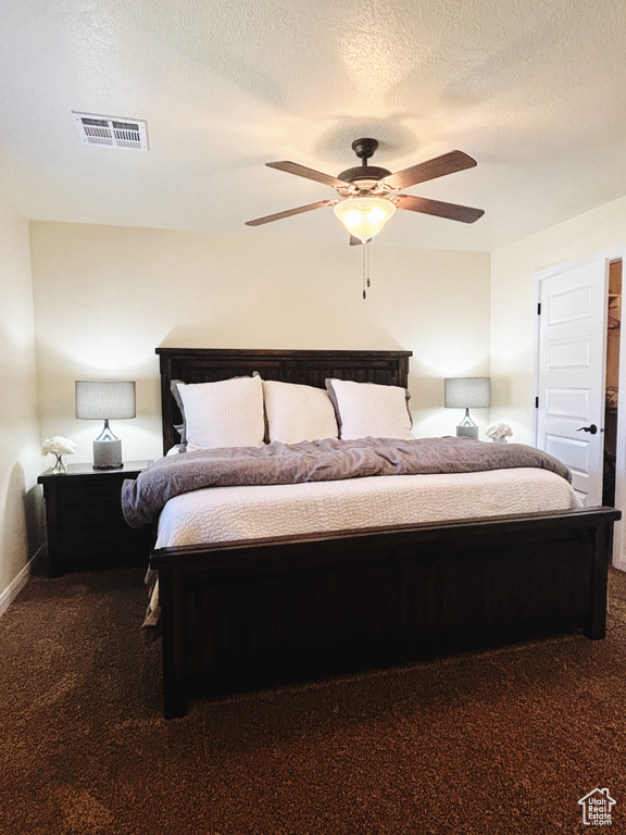 Bedroom with dark colored carpet, ceiling fan, and a textured ceiling