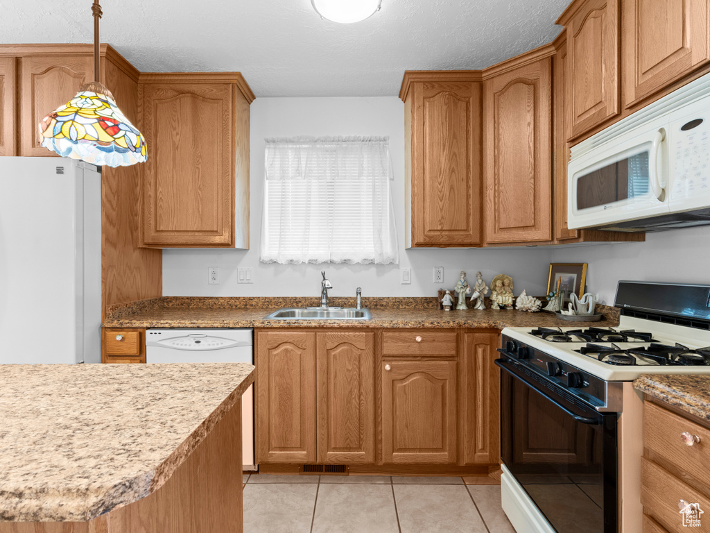 Kitchen featuring white appliances, a sink, light tile patterned floors, and decorative light fixtures