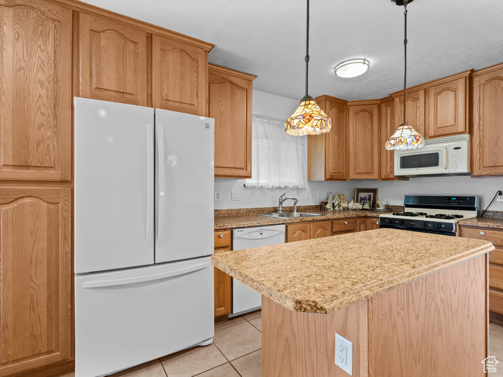 Kitchen featuring white appliances, a sink, light tile patterned floors, hanging light fixtures, and a center island