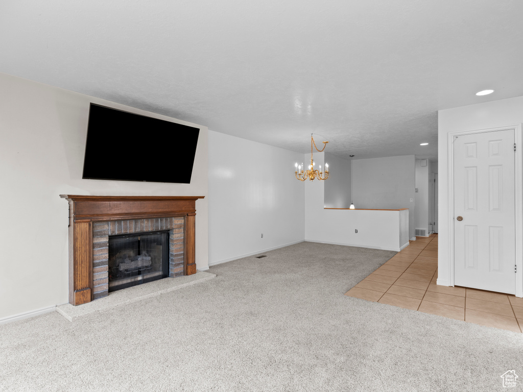 Unfurnished living room with carpet, a chandelier, a fireplace, recessed lighting, and tile patterned floors