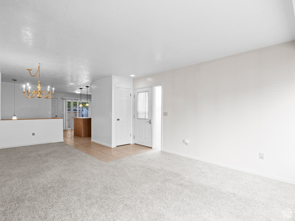 Unfurnished living room featuring a chandelier, light carpet, light tile patterned floors, and baseboards