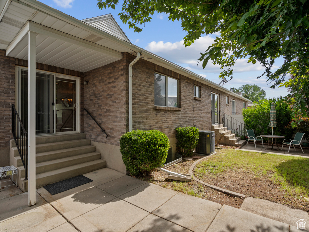 View of exterior entry with brick siding, central air condition unit, and a patio