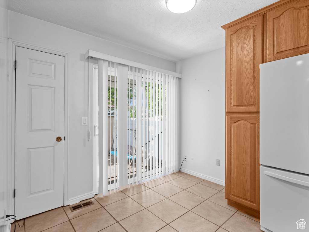 Unfurnished dining area with light tile patterned floors, a textured ceiling, and baseboards