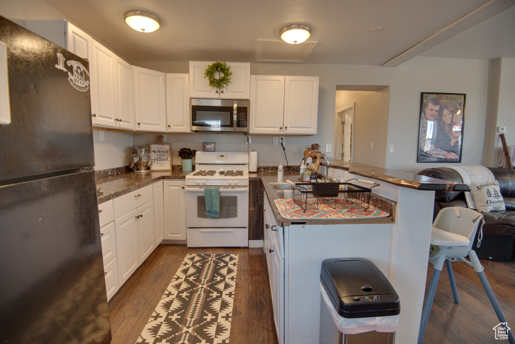Kitchen featuring black fridge, gas range gas stove, dark wood-type flooring, sink, and white cabinetry