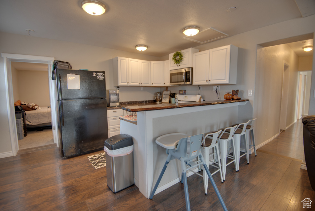 Kitchen with a breakfast bar, black refrigerator, white cabinets, and dark hardwood / wood-style floors