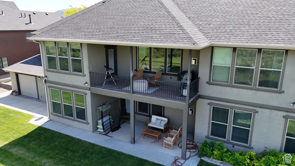 Back of property with stucco siding, a balcony, a patio, and roof with shingles