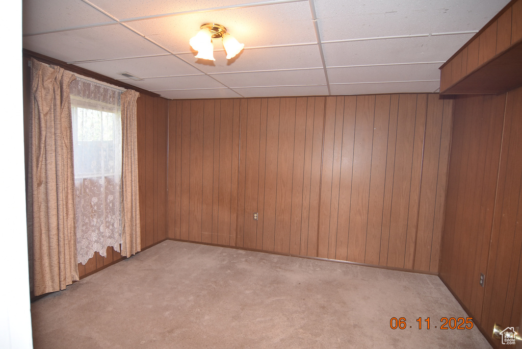 Spare room with a drop ceiling, light carpet, and wood walls