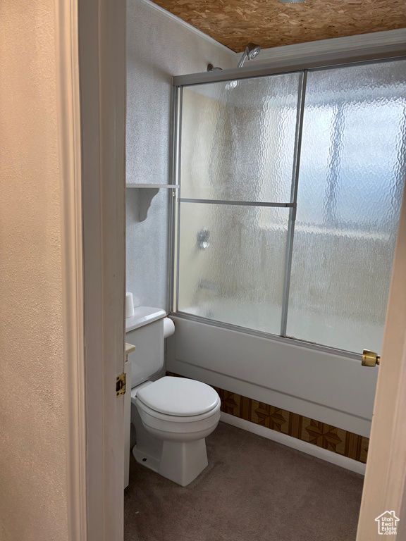 Bathroom with a textured wall, toilet, and bath / shower combo with glass door