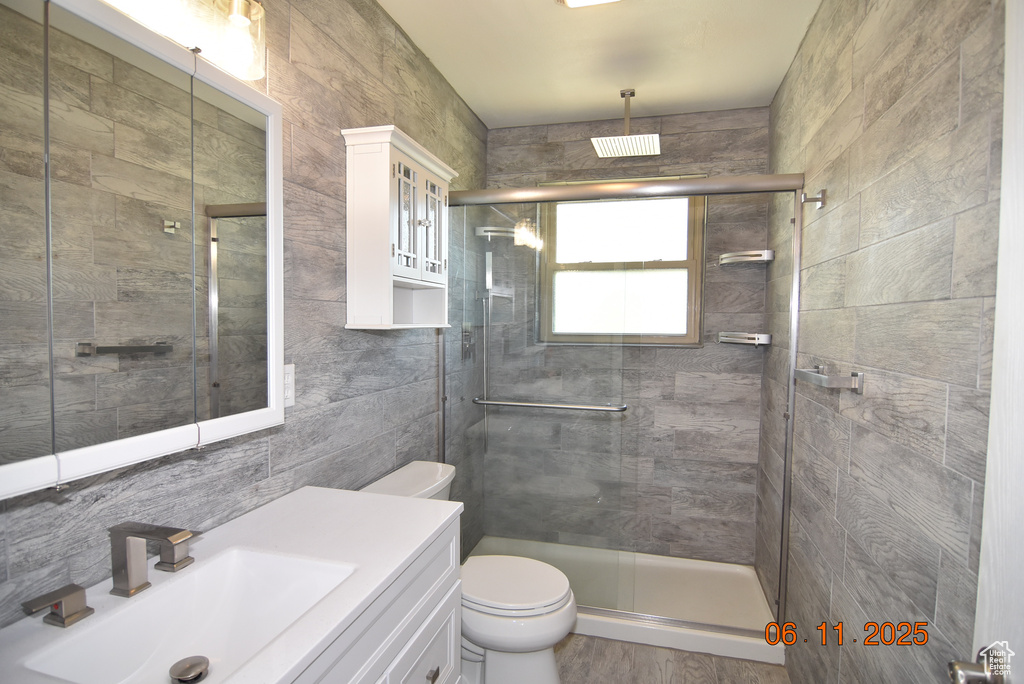 Bathroom with tile walls, a shower stall, and vanity