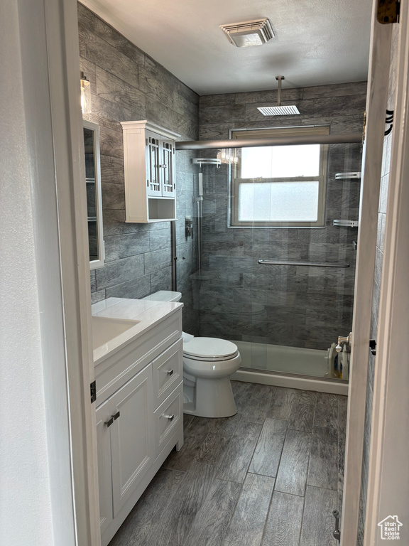 Bathroom featuring visible vents, toilet, a stall shower, vanity, and wood finished floors