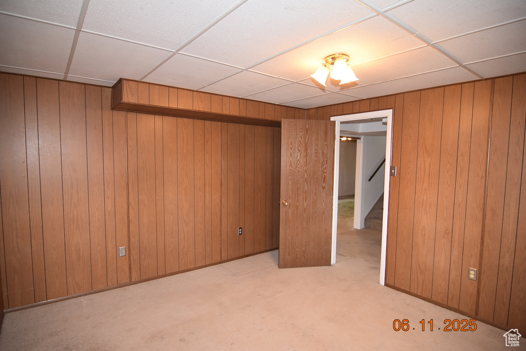 Unfurnished bedroom featuring a paneled ceiling, wooden walls, and carpet