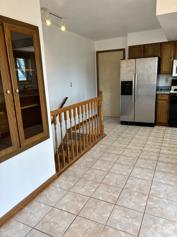 Kitchen featuring white microwave, light tile patterned flooring, range with electric stovetop, baseboards, and stainless steel refrigerator with ice dispenser