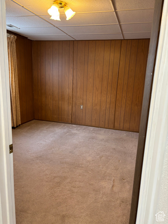 Spare room featuring a drop ceiling, wood walls, and carpet
