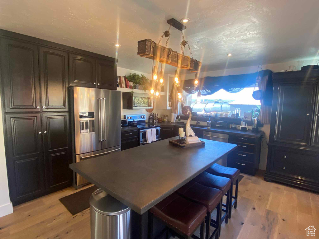 Kitchen featuring appliances with stainless steel finishes, light wood-type flooring, a breakfast bar, a textured ceiling, and decorative light fixtures