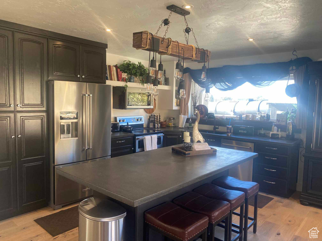 Kitchen with a breakfast bar area, stainless steel appliances, a textured ceiling, and light hardwood / wood-style floors