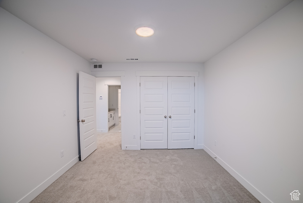 Unfurnished bedroom with baseboards, a closet, visible vents, and light colored carpet