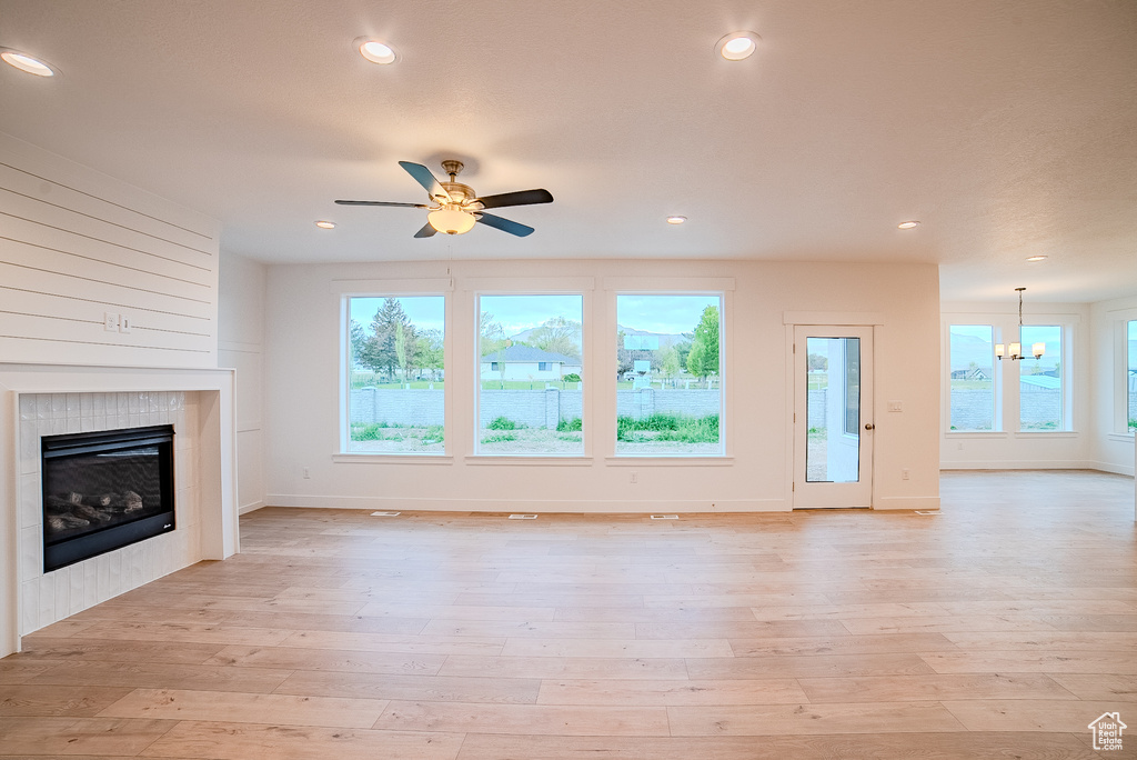 Unfurnished living room featuring a wealth of natural light, a tiled fireplace, baseboards, and ceiling fan with notable chandelier
