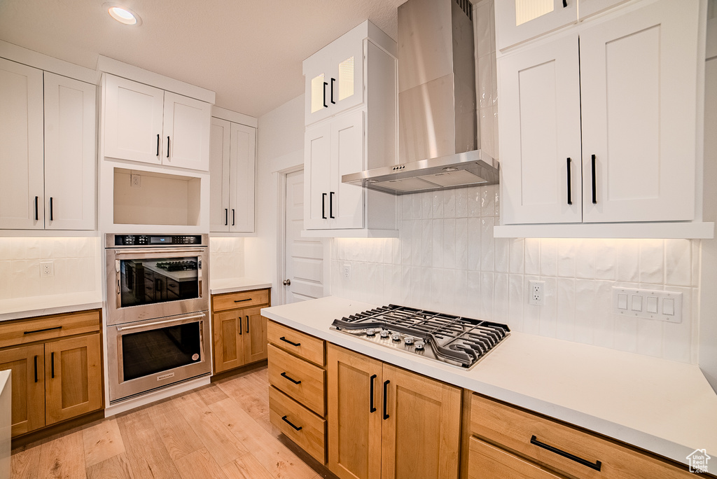 Kitchen featuring wall chimney range hood, light wood-type flooring, stainless steel appliances, and light countertops