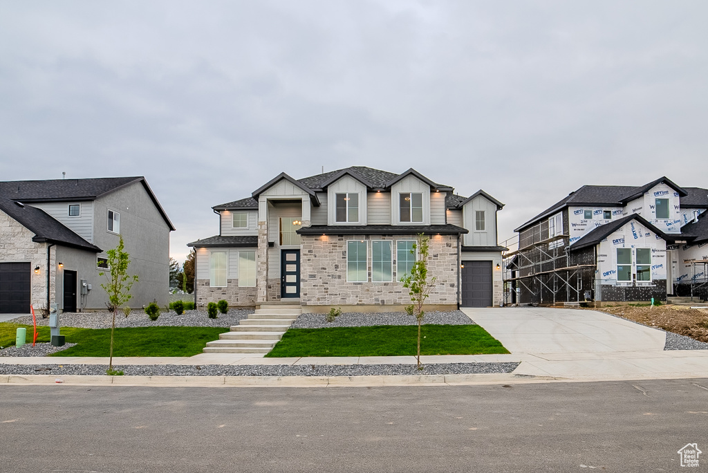 View of front facade featuring an attached garage, board and batten siding, driveway, and a front yard