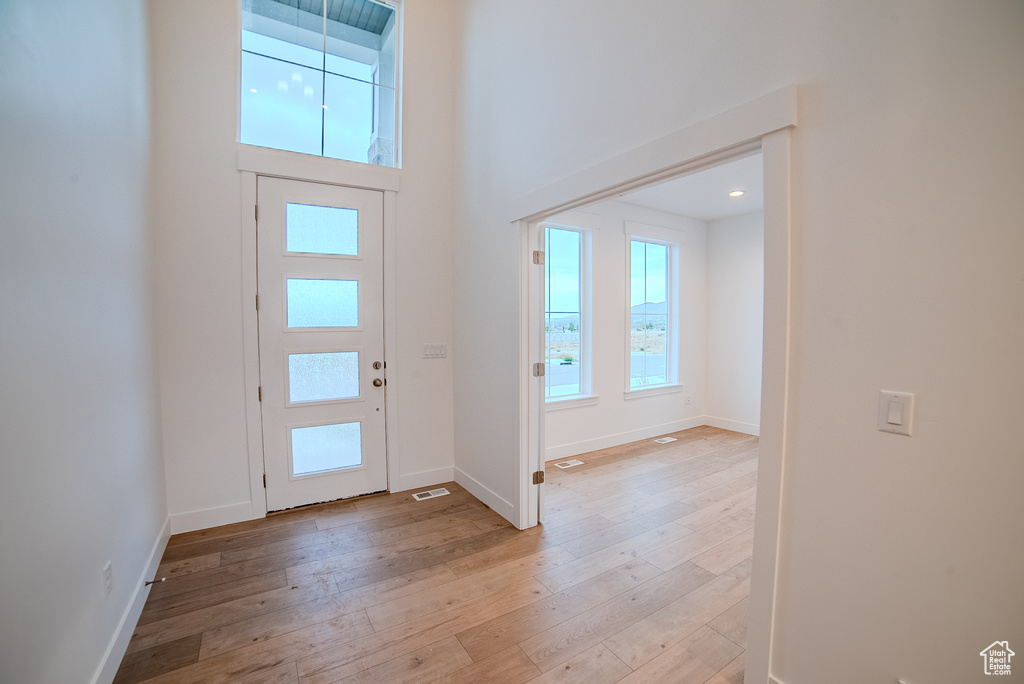 Foyer entrance with light wood-type flooring, baseboards, and a towering ceiling