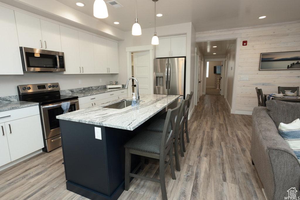 Kitchen featuring a center island with sink, hanging light fixtures, wooden walls, sink, and appliances with stainless steel finishes