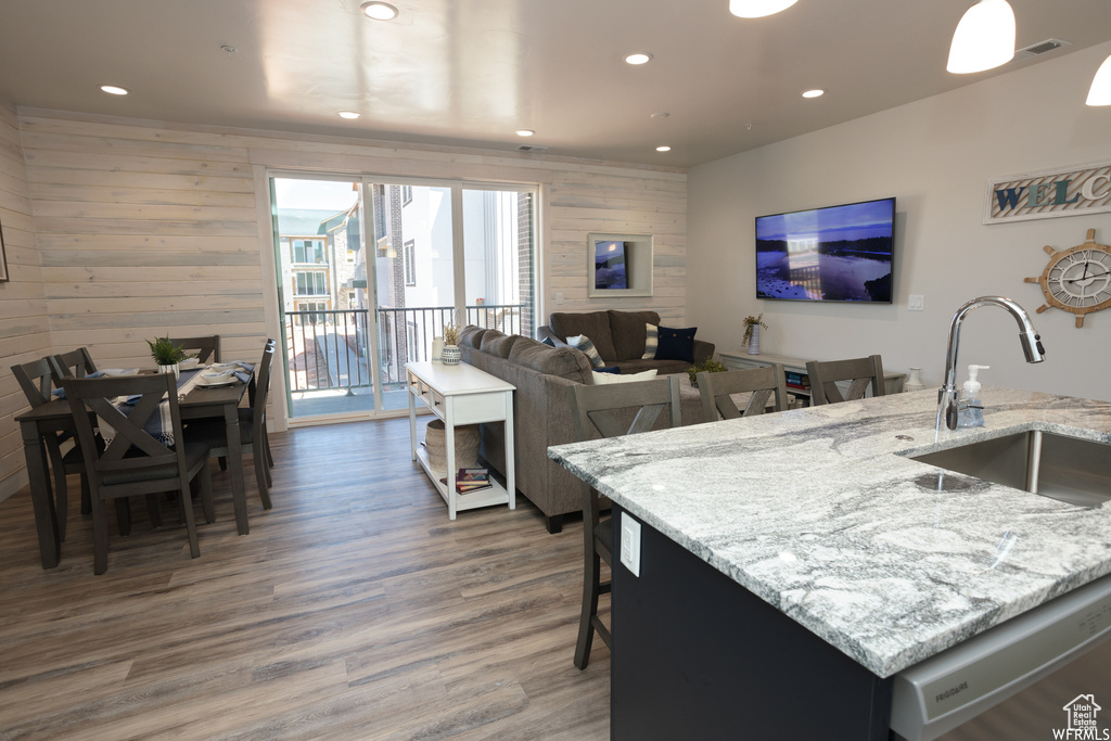 Kitchen featuring light stone counters, a kitchen island with sink, wooden walls, sink, and dark hardwood / wood-style floors
