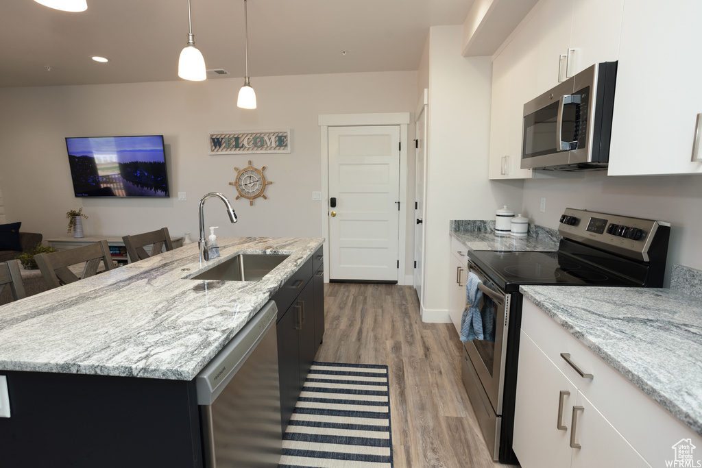 Kitchen with appliances with stainless steel finishes, sink, a center island with sink, white cabinets, and light hardwood / wood-style floors