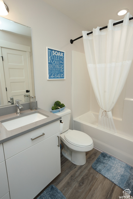Full bathroom featuring hardwood / wood-style floors, vanity, shower / bath combination with curtain, and toilet