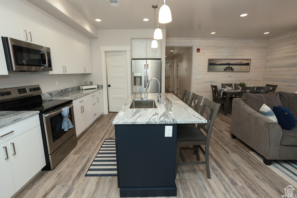 Kitchen with pendant lighting, a breakfast bar, a kitchen island with sink, wooden walls, and appliances with stainless steel finishes