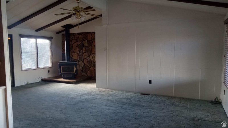 Unfurnished living room featuring lofted ceiling with beams, carpet floors, a wood stove, and ceiling fan