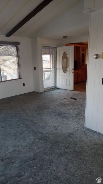 Carpeted spare room featuring vaulted ceiling with beams