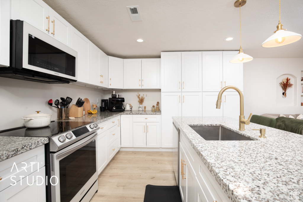 Kitchen featuring light wood-type flooring, stainless steel range with electric stovetop, sink, decorative light fixtures, and white cabinets