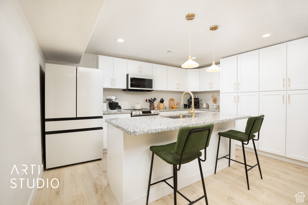 Kitchen featuring white cabinetry, sink, an island with sink, light hardwood / wood-style floors, and white appliances