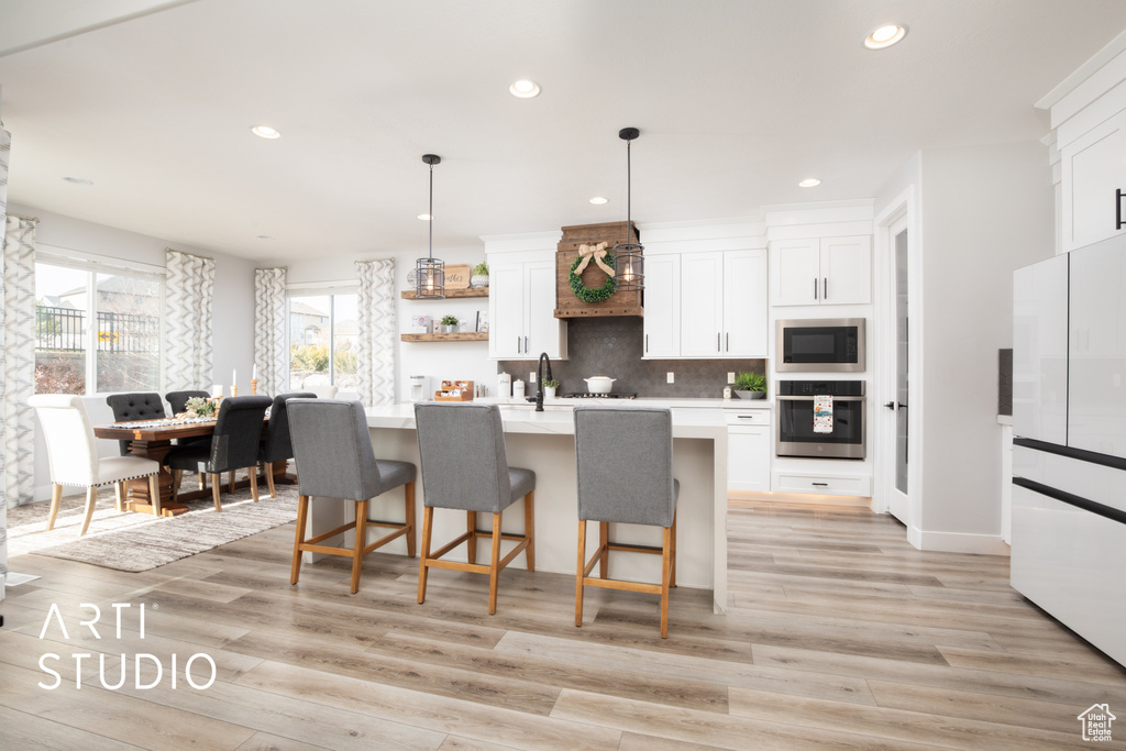 Kitchen with white cabinetry, an island with sink, pendant lighting, and appliances with stainless steel finishes