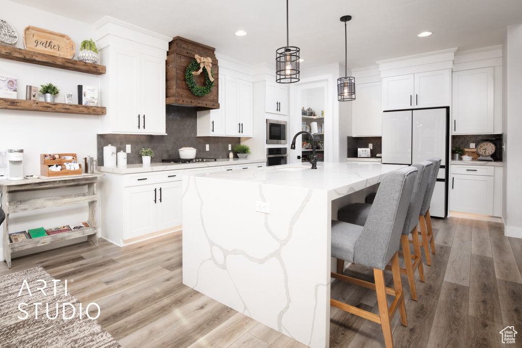 Kitchen with a center island with sink, decorative backsplash, white cabinetry, and light hardwood / wood-style flooring