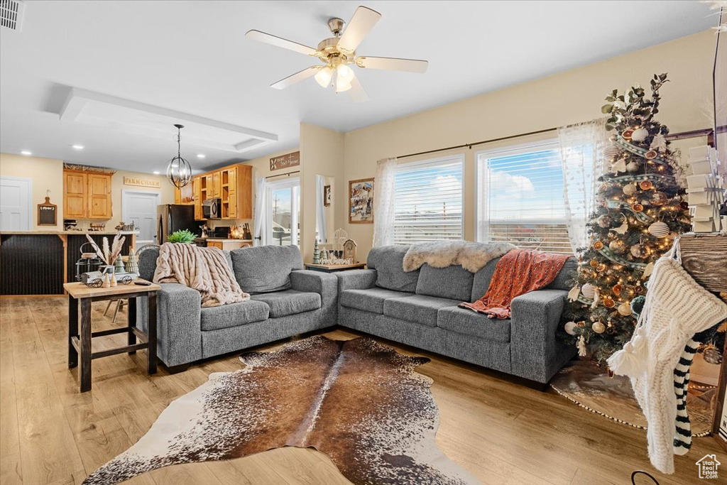 Living room featuring ceiling fan with notable chandelier and light wood-type flooring