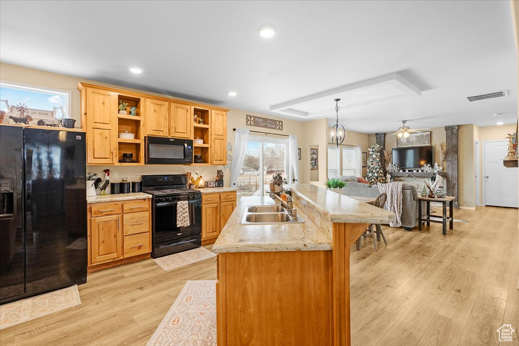 Kitchen with sink, black appliances, decorative light fixtures, and light wood-type flooring