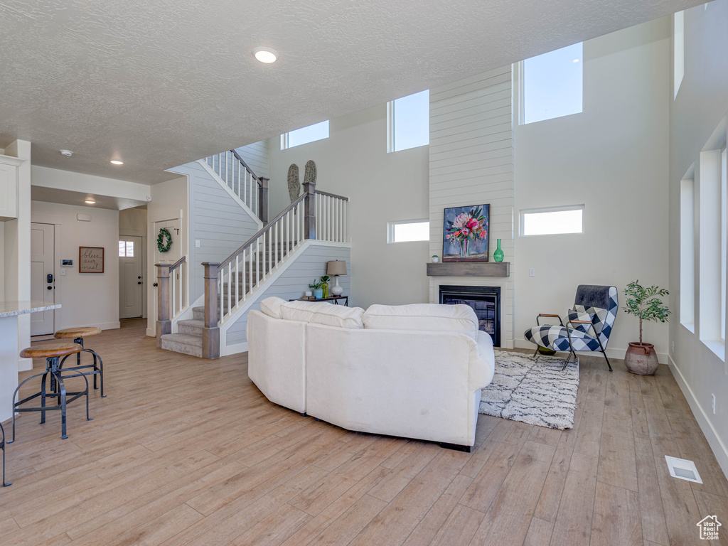 Living room featuring a textured ceiling, visible vents, light wood finished floors, a fireplace, and stairway