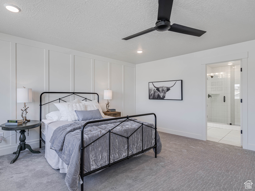 Carpeted bedroom with a decorative wall, connected bathroom, ceiling fan, and a textured ceiling