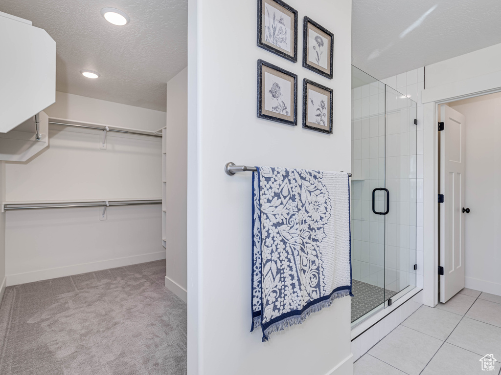 Bathroom featuring a shower stall, a spacious closet, a textured ceiling, tile patterned flooring, and baseboards