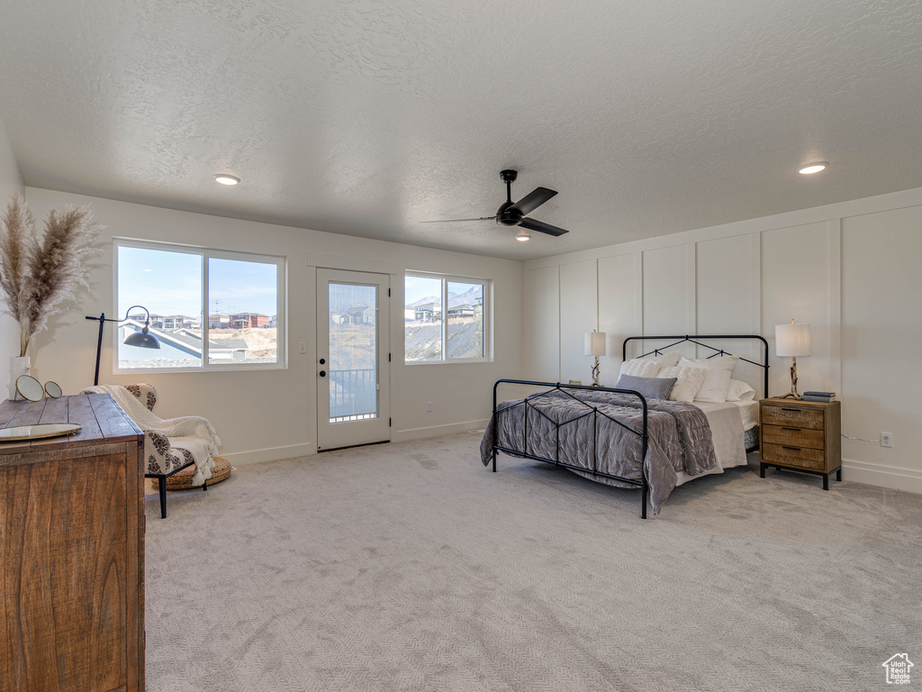 Bedroom featuring light colored carpet, a textured ceiling, a decorative wall, and access to outside
