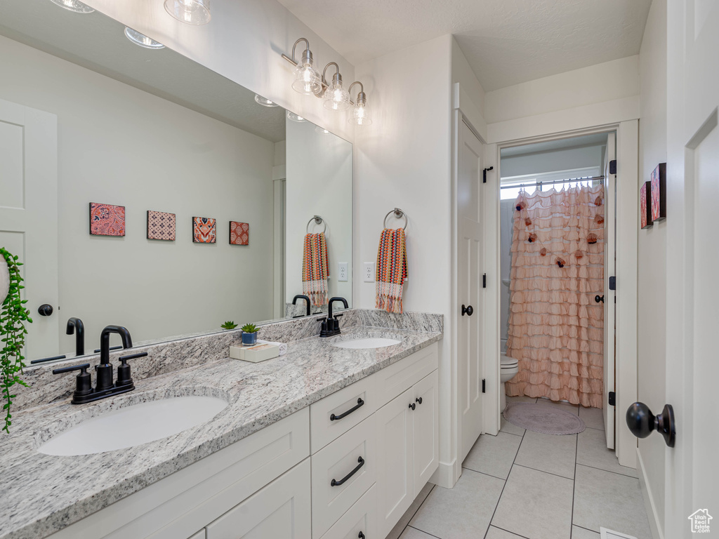Full bathroom featuring double vanity, toilet, tile patterned flooring, and a sink