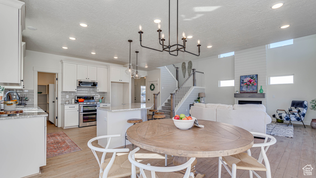 Dining area featuring stairs, light wood-style floors, a large fireplace, and a textured ceiling